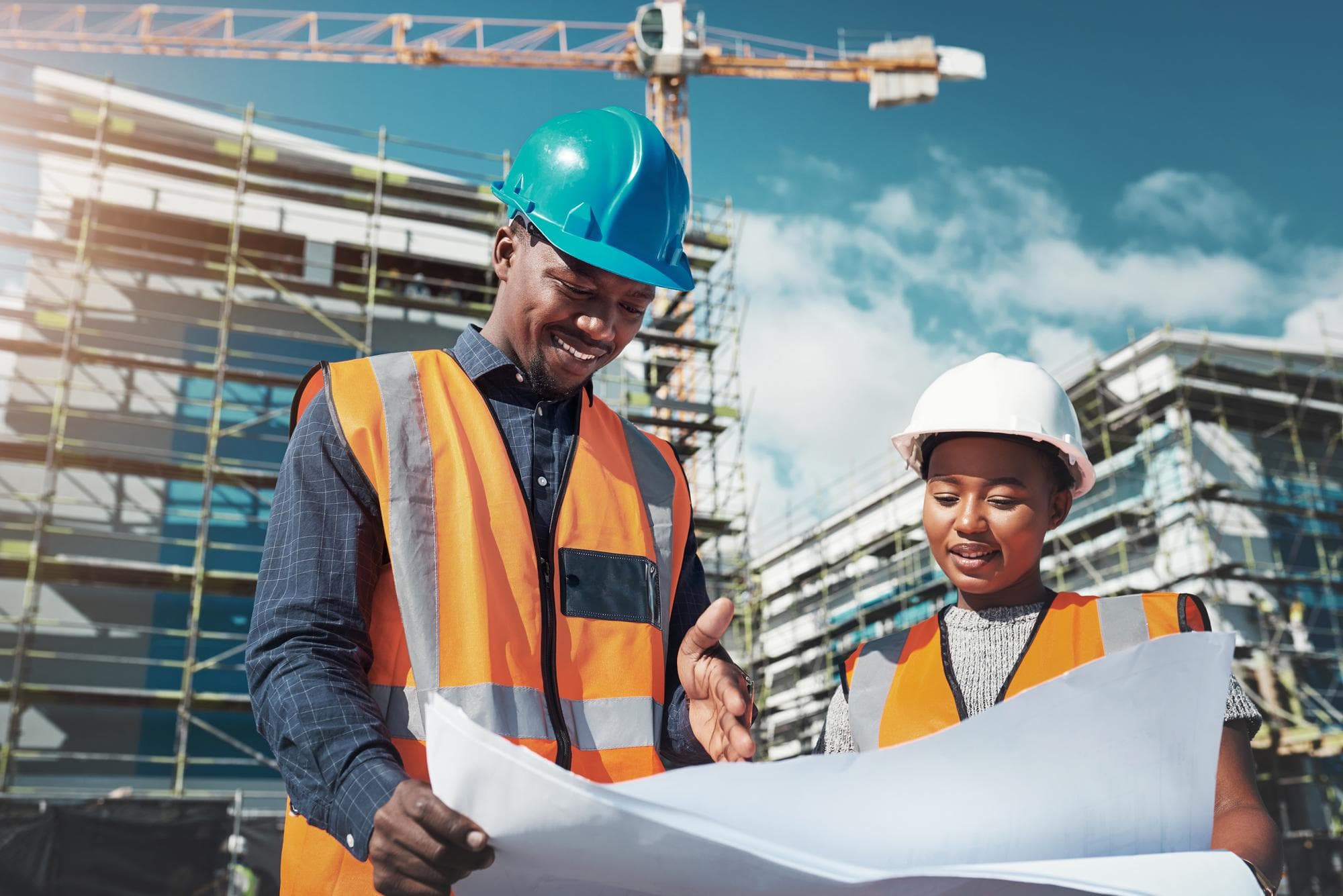 Two site engineers in hard hats reviewing construction drawings